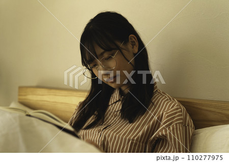 ベッドで本を読みながら寝てしまう若い女性 110277975