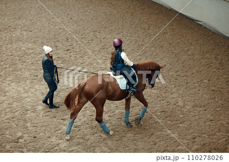 Aerial, top view. Female teacher, instructor teaching little girl, kid horseback riding. Education, animal sport 110278026