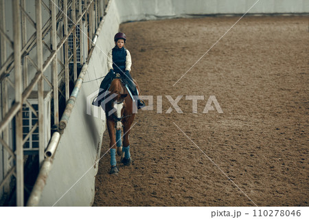 Concentrated little girl in inform and special clothes siting on horse, training horseback riding on special manege Concentrated little girl in inform and special clothes siting on horse, training horseback riding on special manege 110278046