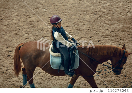 Concentrated little girl in inform and special clothes siting on horse, training horseback riding on special manege Concentrated little girl in inform and special clothes siting on horse, training horseback riding on special manege 110278048
