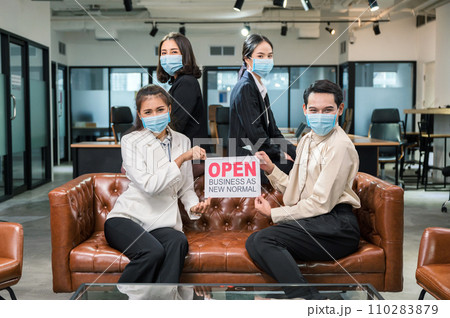 Young asian business team wearing face mask with placard open business as new normal on leather sofa in coworking space 110283879