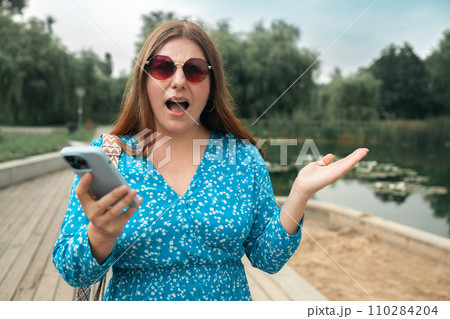 Surprised young Caucasian woman in stylish dresses using a mobile phone and looking smartphone screen outdoors at sunny day. High quality photo Surprised young Caucasian woman in stylish dresses using a mobile phone and looking smartphone screen outdoors at sunny day. High quality photo 110284204