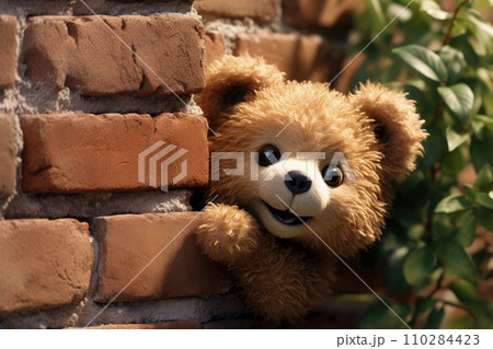 A funny bear doll peeks out from behind an old red brick wall 110284423