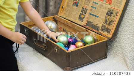 Children and mother put New Year's toys in an old suitcase. Close-up of hands putting New Year's toys into a box. Concept of the end of winter holidays and New Year, Christmas. Children and mother put New Year's toys in an old suitcase. Close-up of hands putting New Year's toys into a box. Concept of the end of winter holidays and New Year, Christmas. 110287438