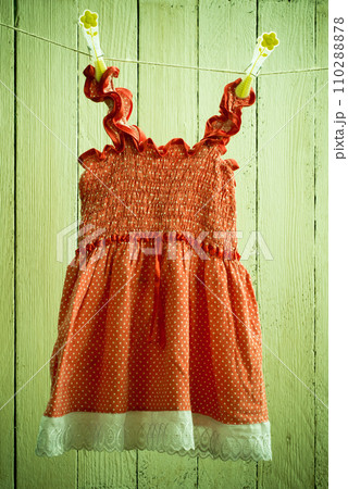 Old washed baby dress red with white polka dots hanging on the clothesline Old washed baby dress red with white polka dots hanging on the clothesline 110288878