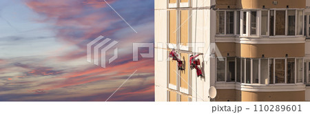 Repair work at height (sealing seams in a panel house), against the sky at sunset. Worker insulates the seams of the facade of an old residential building. Maintenance of residential buildings Repair work at height (sealing seams in a panel house), against the sky at sunset. Worker insulates the seams of the facade of an old residential building. Maintenance of residential buildings 110289601