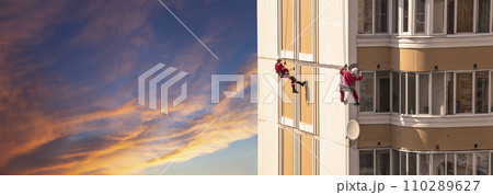Repair work at height (sealing seams in a panel house), against the sky at sunset. Worker insulates the seams of the facade of an old residential building. Maintenance of residential buildings 110289627
