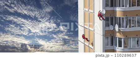 Repair work at height (sealing seams in a panel house), against the sky with clouds. Worker insulates the seams of the facade of an old residential building. Maintenance of residential buildings Repair work at height (sealing seams in a panel house), against the sky with clouds. Worker insulates the seams of the facade of an old residential building. Maintenance of residential buildings 110289637