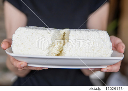 A hand holds a piece of cottage cheese close-up. Eating tasty and healthy foods. A hand holds a piece of cottage cheese close-up. Eating tasty and healthy foods. 110291384