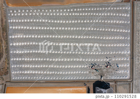 Aerial top view of farmers making heaps of raw sea salt piles with sea. Farm field outdoor. Nature material in traditional salt industry in Thailand. Asia culture. Agriculture lifestyle people 110291528