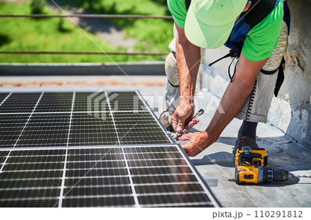 Worker building photovoltaic solar panel system on rooftop of house. Man engineer installing solar module with help of wrench outdoors. Alternative and renewable energy generation concept. Worker building photovoltaic solar panel system on rooftop of house. Man engineer installing solar module with help of wrench outdoors. Alternative and renewable energy generation concept. 110291812