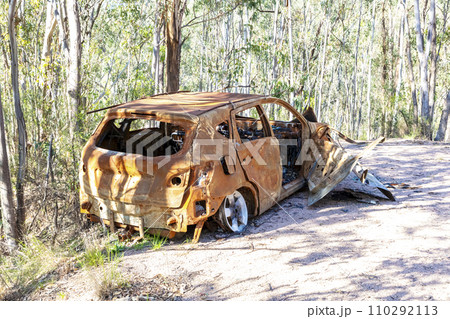 A small car left on a dirt road in a forest that has been burnt out and destroyed A small car left on a dirt road in a forest that has been burnt out and destroyed 110292113