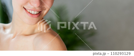 Anonymous smiling woman with bare shoulder posing after shower, with copy space. Crop view of happy young female with soft fresh skin, against blurred grey background. Purity, femininity concept. Anonymous smiling woman with bare shoulder posing after shower, with copy space. Crop view of happy young female with soft fresh skin, against blurred grey background. Purity, femininity concept. 110293129