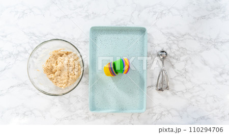 Flat lay. Scooping cupcake batter with dough scoop into silicon muffin liners to lemon poppy seed muffins. 110294706