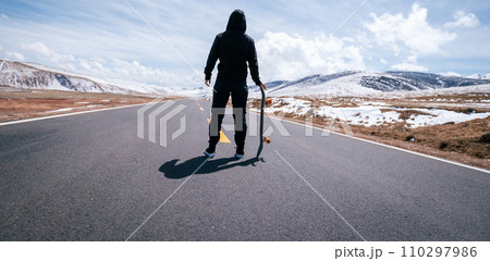 Skateboarder skateboarding on snowy country road 110297986