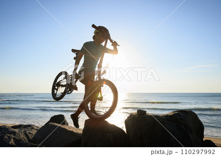 Woman carrying a folding bike on sunrise seaside Woman carrying a folding bike on sunrise seaside 110297992