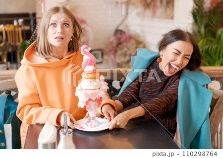 Two women cannot share dessert in form pink flamingo in cafe, they push plate Two women cannot share dessert in form pink flamingo in cafe, they push plate 110298764
