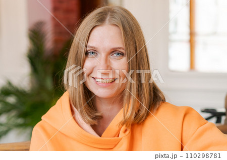 Portrait happy woman in cafe. Wearing a bright orange sweatshirt. 110298781