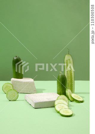 Fresh cucumbers positioned alongside two stone platforms on a pastel green backdrop. Front-view presentation with vacant space for product display, embodying the concept of cucumber benefits. 110300508