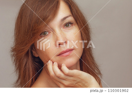 Portrait of cropped caucasian middle aged woman face with freckles holding fingers on cheek Portrait of cropped caucasian middle aged woman face with freckles holding fingers on cheek 110301902