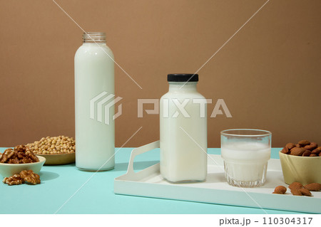 Ceramic bowls and dish containing almond, walnuts and soybeans arranged with a cup and bottles of milk. Nuts and beans are largely composed of fats 110304317