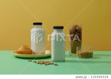 Two empty label bottles of fresh milk decorated with a cake and glasses of soybeans, almond and walnuts. Yellow background. Healthy organic food concept 110304329