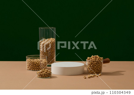 Several glasses filled with soybeans are displayed around an empty podium. Mock-up for exhibitions or presentation of cosmetic products or packaging Several glasses filled with soybeans are displayed around an empty podium. Mock-up for exhibitions or presentation of cosmetic products or packaging 110304349