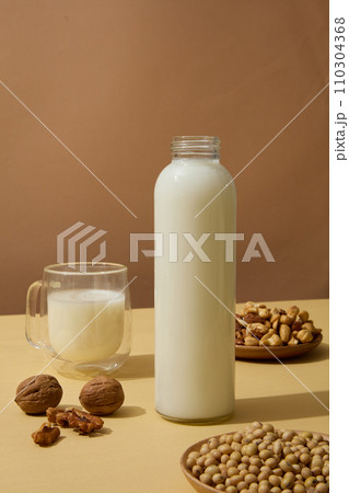 Wooden dishes of soybeans, cashew nuts and walnuts displayed on beige surface with containers of milk. Nuts are a great source of several nutrients, including vitamin E 110304368