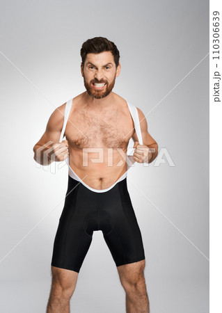 Angry bearded wrestler in black and white singlet, while posing to camera. Front view of aggressive athlete making face, showing rage, isolated on white studio background. Concept of wrestling. 110306639