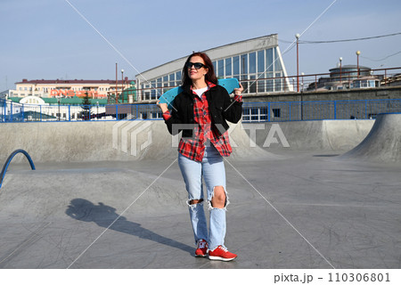 An active middle-aged woman rides a skateboard on an empty road or highway. An ordinary city woman relaxing on a skateboard after work. The concept of a modern lifestyle An active middle-aged woman rides a skateboard on an empty road or highway. An ordinary city woman relaxing on a skateboard after work. The concept of a modern lifestyle 110306801