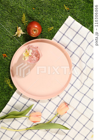 On a green grass background and checkered fabric, pink flowers and pinks dish displayed. Blank space on dish for display product. Top view, picnic on holiday On a green grass background and checkered fabric, pink flowers and pinks dish displayed. Blank space on dish for display product. Top view, picnic on holiday 110306866