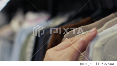 Woman hand runs across a rack of clothes at house or store. Home wardrobe or clothing shop changing room. 110307388