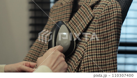 Woman steams plaid jacket with electric steamer at home. Dry cleaning clothes. Household and home equipment for housework. 110307400