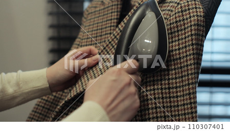 Woman steams plaid jacket with electric steamer at home. Dry cleaning clothes. Household and home equipment for housework. 110307401