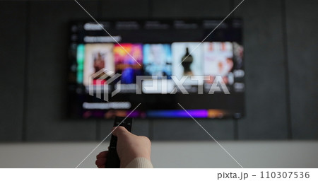 Woman hand operating a remote control for a smart TV. Channel surfing, focused on the hand and remote control. Woman hand operating a remote control for a smart TV. Channel surfing, focused on the hand and remote control. 110307536