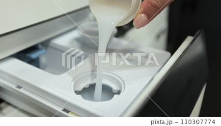 Pour laundry gel softener to smell good into the washing machine container. Using fabric softener for laundry. Household chores concept. Pour laundry gel softener to smell good into the washing machine container. Using fabric softener for laundry. Household chores concept. 110307774