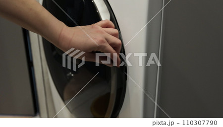 Woman pulls clean washed clothing from the washing machine. Washing clothing in domestic washing machine. Woman pulls clean washed clothing from the washing machine. Washing clothing in domestic washing machine. 110307790
