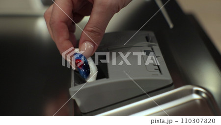 Close up of woman hands puts detergent dishwasher tablet In dishwasher machine. Modern home kitchen. Easy housekeeping domestic life. 110307820