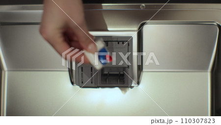 Close-up, top view. Woman putting an all in one detergent capsule pill into a dishwasher. 110307823