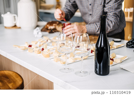 Wine Tasting Preparation with Cheese Pairings. Sommelier prepares for a wine tasting event, carefully pairing various cheeses with wines, featuring an unopened bottle and elegant glasses. Wine Tasting Preparation with Cheese Pairings. Sommelier prepares for a wine tasting event, carefully pairing various cheeses with wines, featuring an unopened bottle and elegant glasses. 110310419