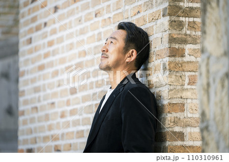レンガの壁にもたれる50代半ばの男性　ポートレート 110310961