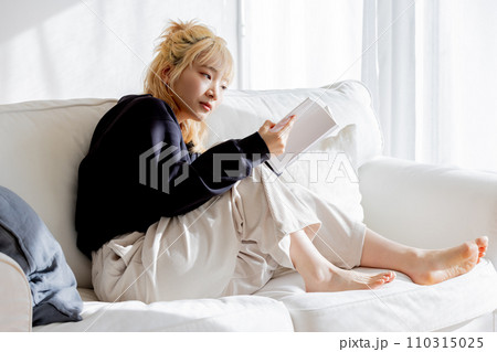 ソファーに座り本を読む金髪の女性 110315025