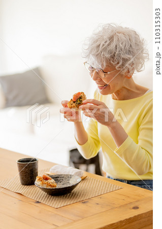 ふわふわのおにぎりを食べるシニア女性 110315303