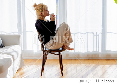 椅子に座りコーヒーを飲む金髪の女性 110315554