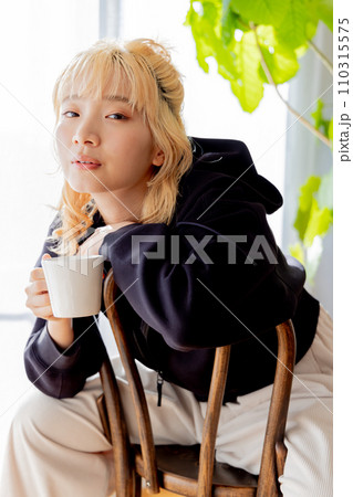 椅子に後ろ向きに座りコーヒーを飲む金髪の女性 110315575