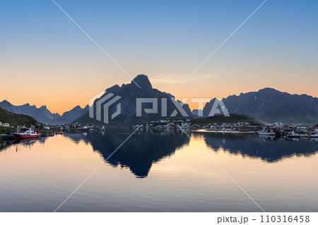Serene fjord reflects rugged peaks as a Lofoten village awakens to sunrise hues 110316458
