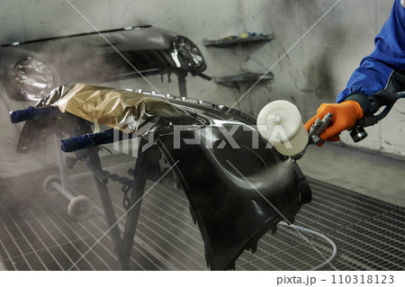 The photograph captures the scene of an automotive workshop, showcasing the process of painting various car parts. Different components of the vehicle car bonnet, bumpers, smaller details. The photograph captures the scene of an automotive workshop, showcasing the process of painting various car parts. Different components of the vehicle car bonnet, bumpers, smaller details. 110318123