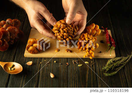 The cook prepares fresh velvet stem mushrooms with aromatic spices on the kitchen table. Sorting velvet foot or flammulina velutipes by the hands of a chef 110318196