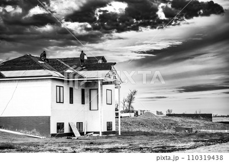 Shingle roof being installed on a two-story walkout new build residential construction house. Shingle roof being installed on a two-story walkout new build residential construction house. 110319438