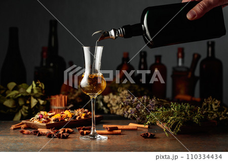 Yellow herbal liquor or balm is poured from a vintage bottle into a glass. 110334434